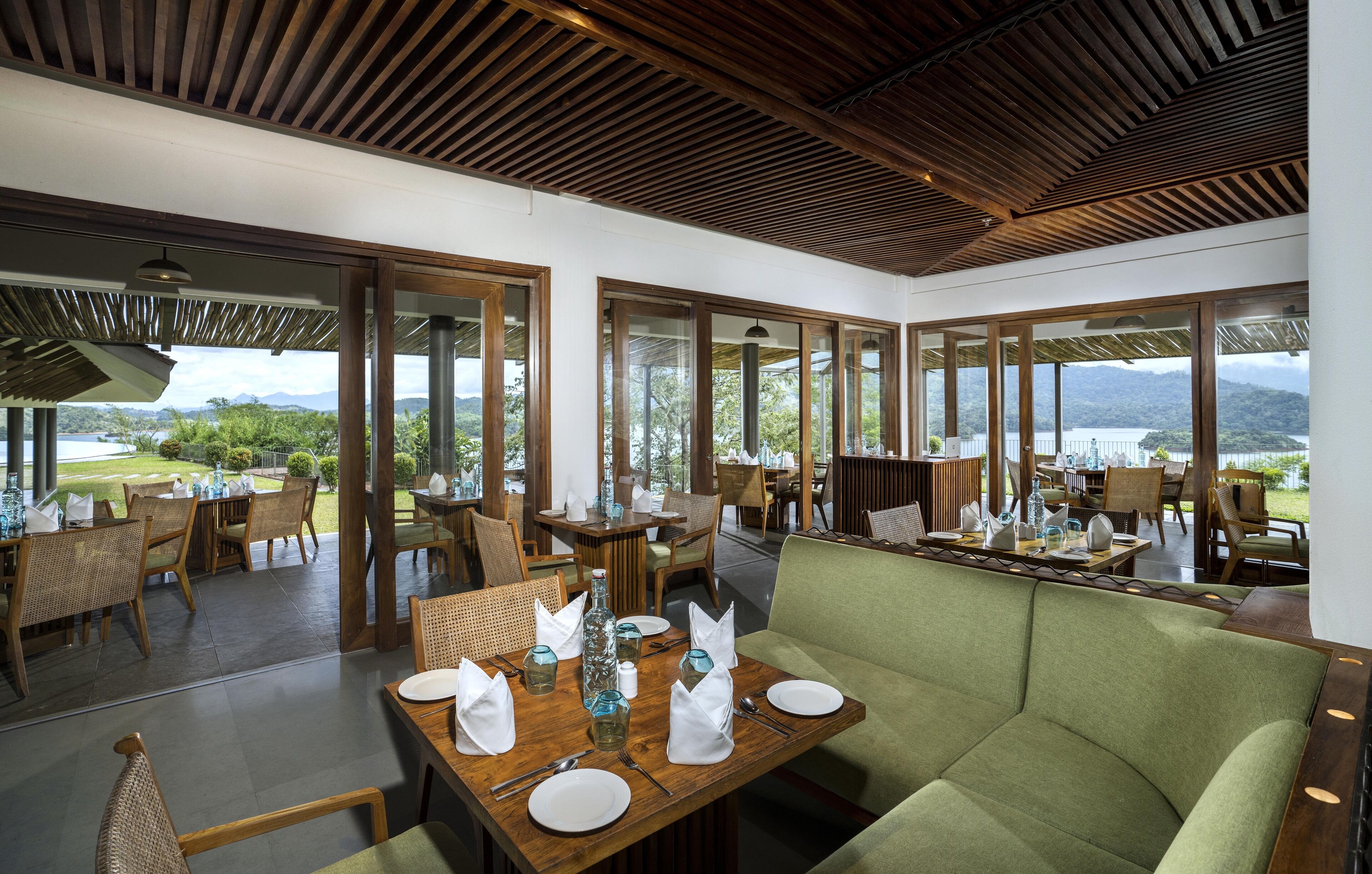 A restaurant with wooden furniture, large windows, and a view of a lake and mountains.