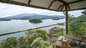 Un balcón con vistas a un lago, montañas y una edificación con techo de paja.