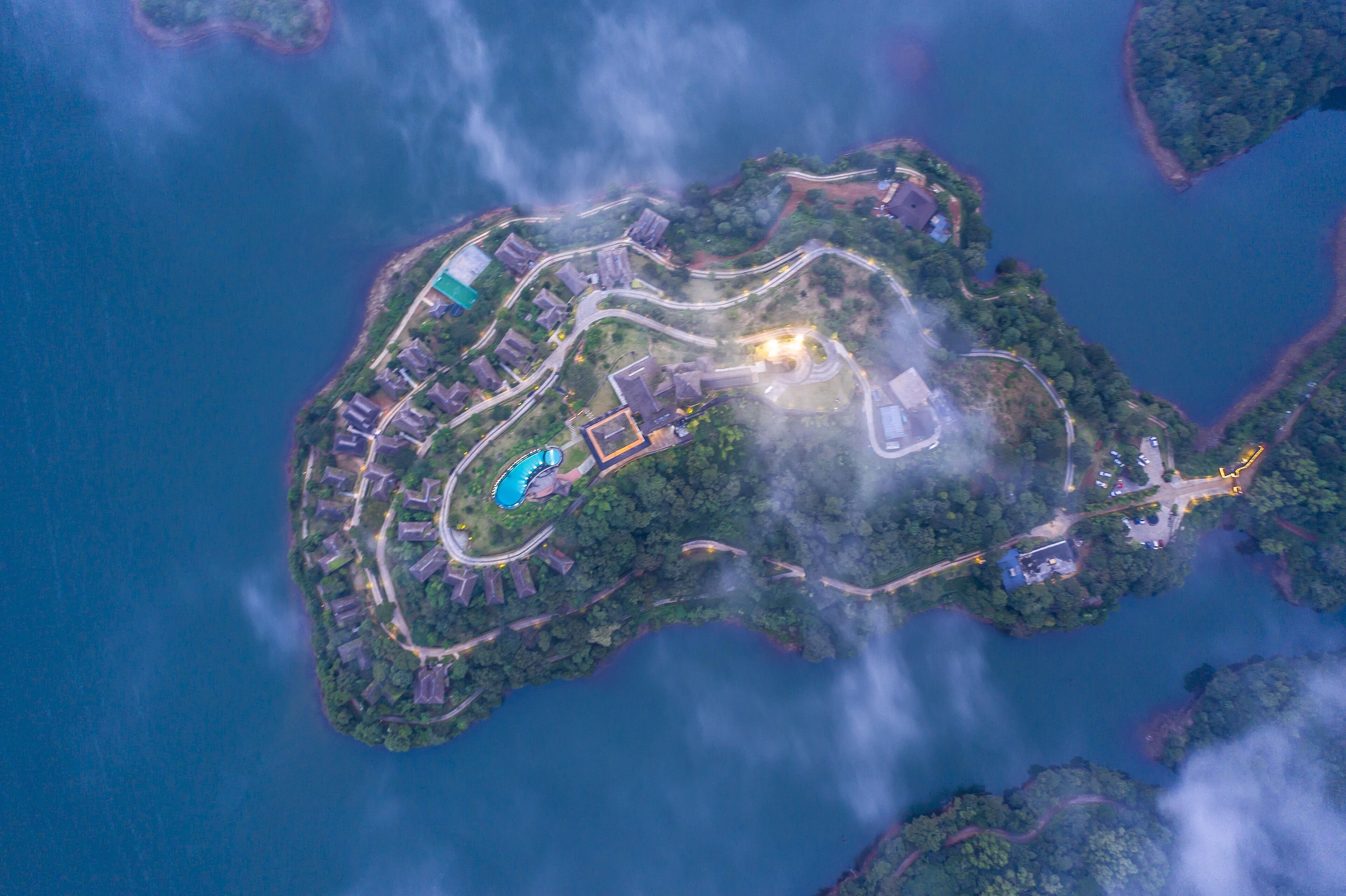 Vista aérea de uma ilha costeira com uma estrada sinuosa, piscina e edifícios residenciais.