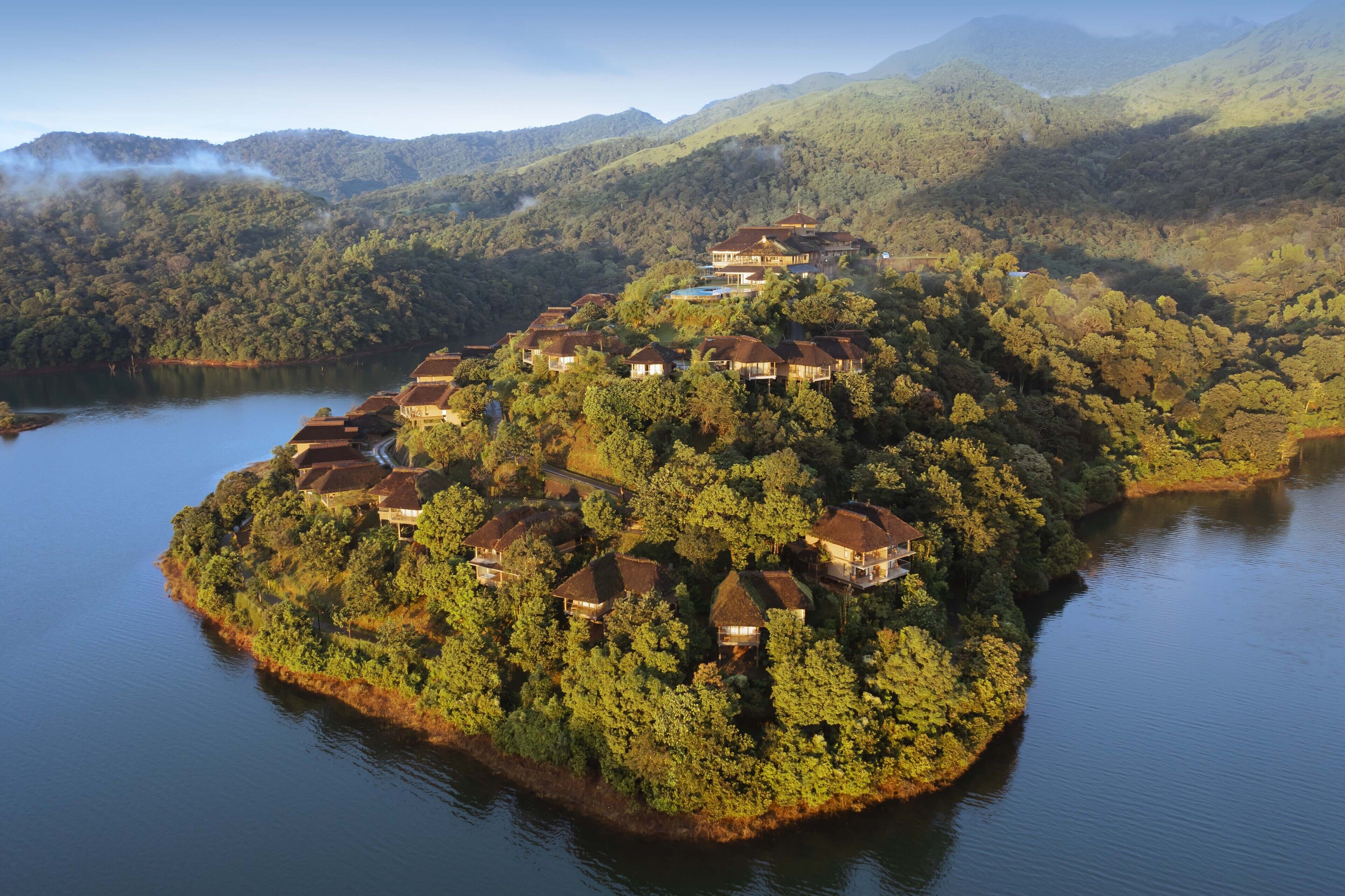 A cluster of houses on a forested island surrounded by water, with mountains in the background.