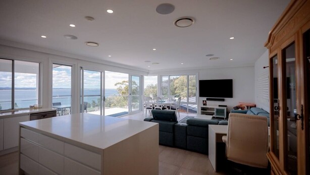 A modern kitchen with a large island, a dining area with a view, and a living space with a flat-screen TV. - Spectacular water views & entertaining spaces (Corlette)
