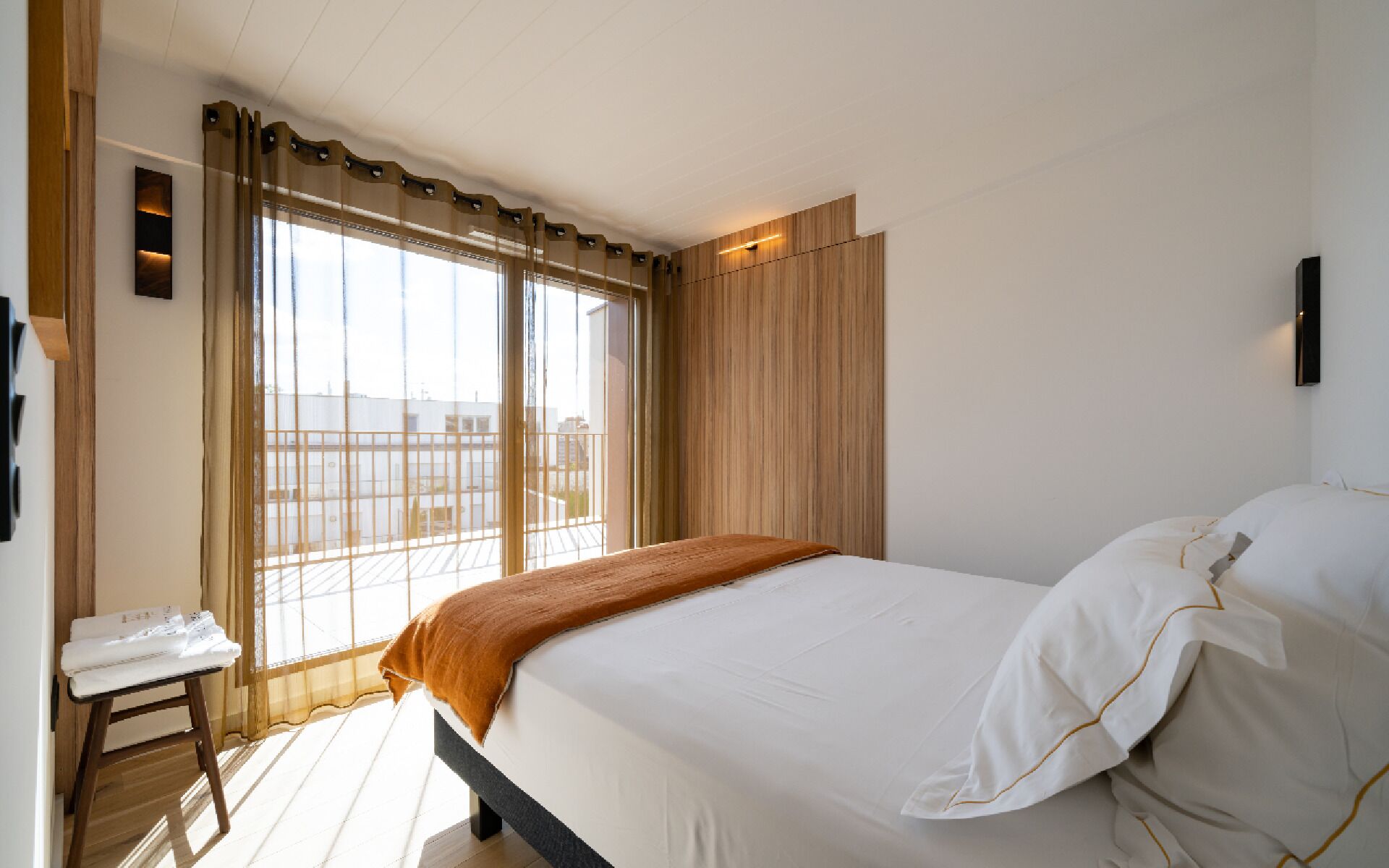 Habitación de hotel con cama, una mesita con teléfono, ventana con cortinas y vistas al exterior.