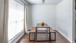 Una habitación con una mesa de madera, bancos, un jarrón con flores y una ventana con cortinas.