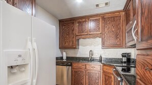 Una cocina con armarios de madera, un refrigerador blanco, un lavavajillas de acero inoxidable y una encimera de granito.