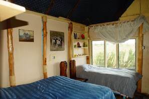 Two single beds with blue and white striped bedspreads, a shelf unit, and artwork adorn this cozy space.