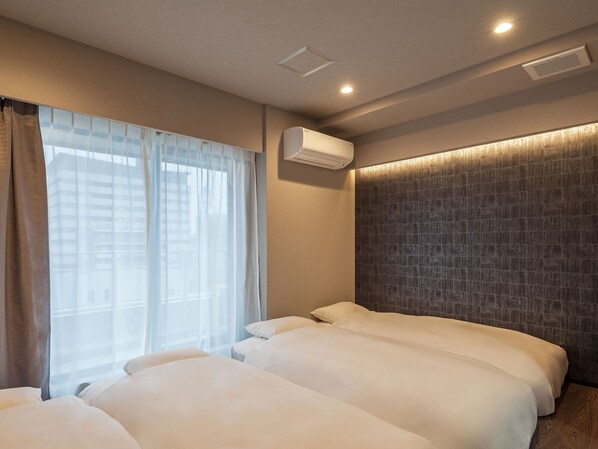 Habitación de hotel con dos camas, un ventanal con cortinas translúcidas, un equipo de aire acondicionado y una pared con textura.