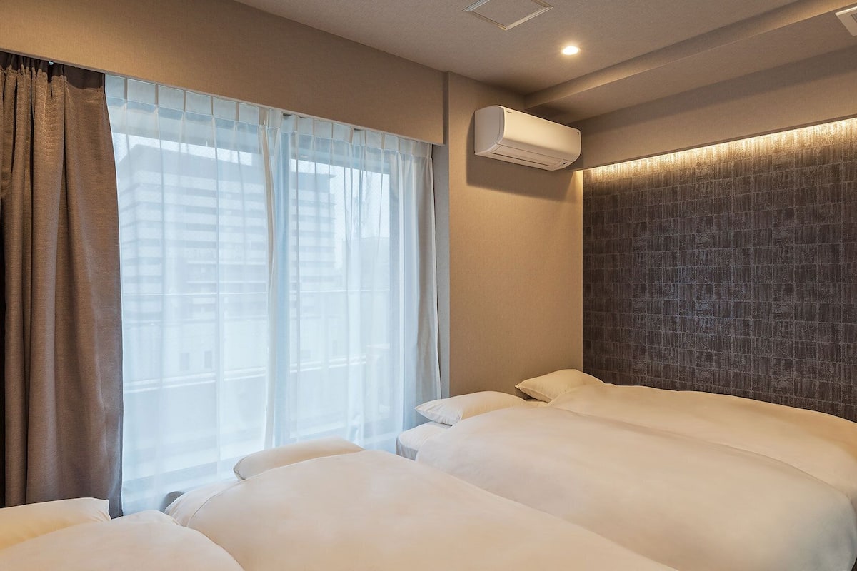 Une chambre d’hôtel avec deux lits, une fenêtre avec des rideaux légers, un appareil de climatisation et un mur à texture.