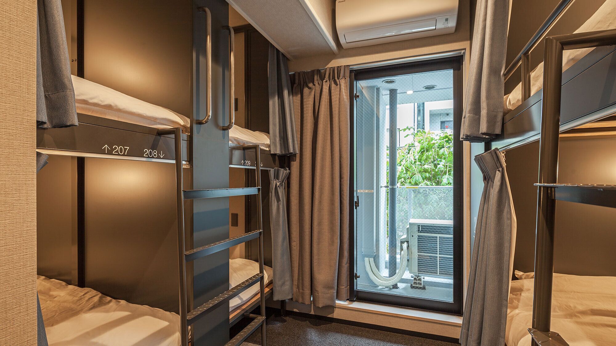 Una habitación de hotel compacta con literas, una ventana con cortinas y un equipo de aire acondicionado.