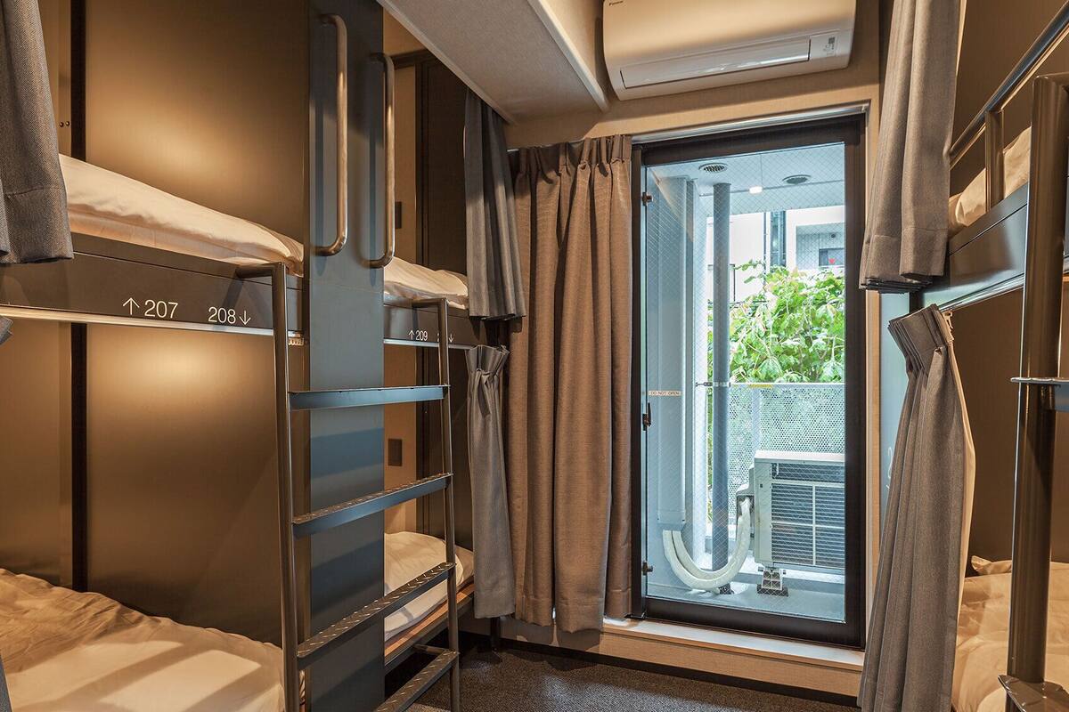 Una habitación de hotel compacta con literas, una ventana con cortinas y un equipo de aire acondicionado.