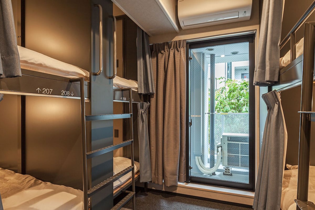 Una habitación de hotel compacta con literas, una ventana con cortinas y un equipo de aire acondicionado.