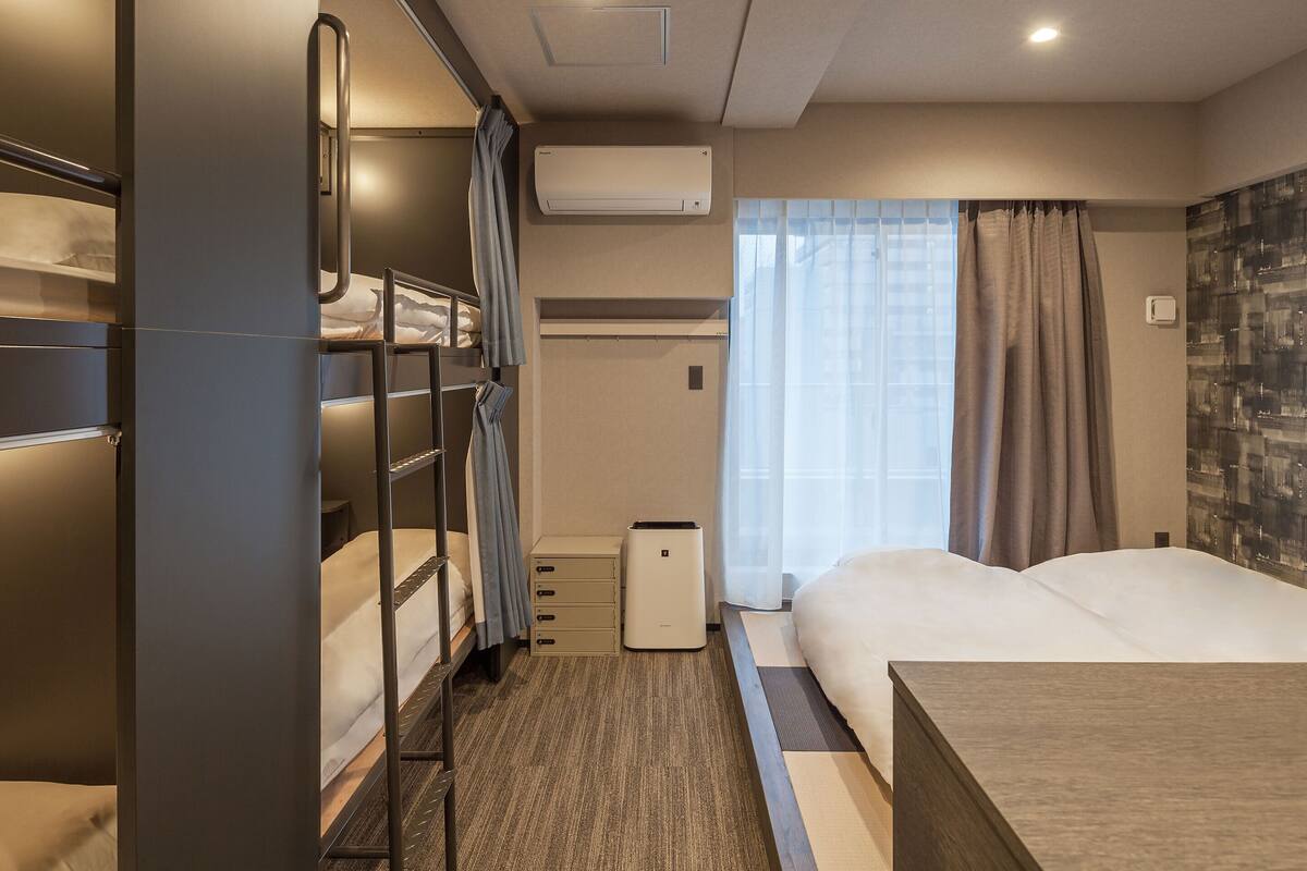 Una habitación de hotel con literas, un escritorio, una mesita de noche y una ventana con cortinas.