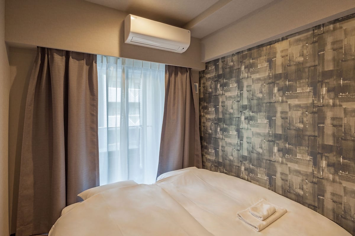 Una habitación de hotel con cama, aire acondicionado, ventana con cortinas y pared con diseño.