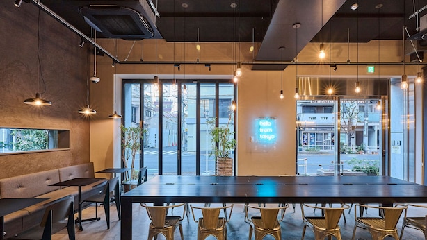 A modern interior with a long table and chairs, large windows, and hanging pendant lights. - Hotel Plus Hostel TOKYO AKIHABARA (Tokyo)