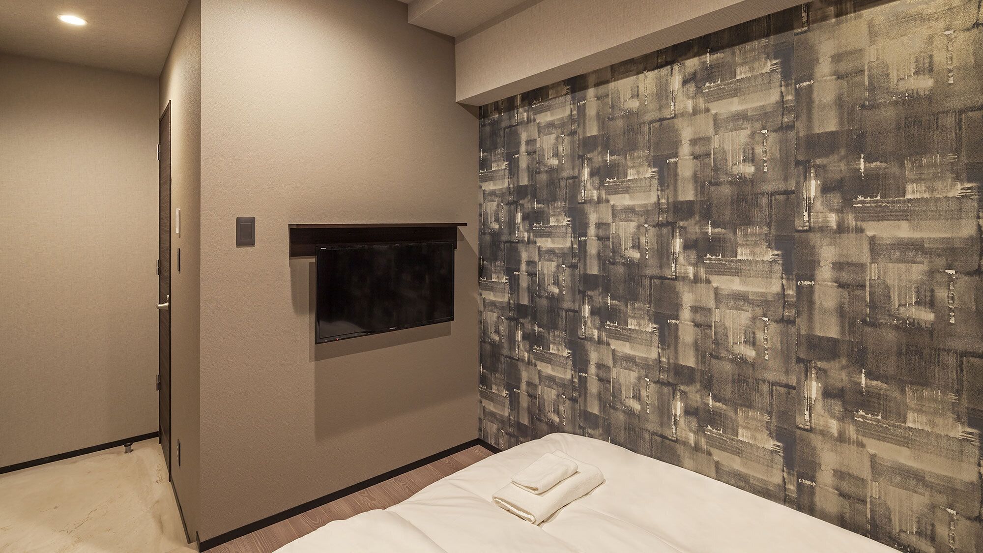 A hotel room with a bed, a flat-screen TV mounted on the wall, and a patterned wall.