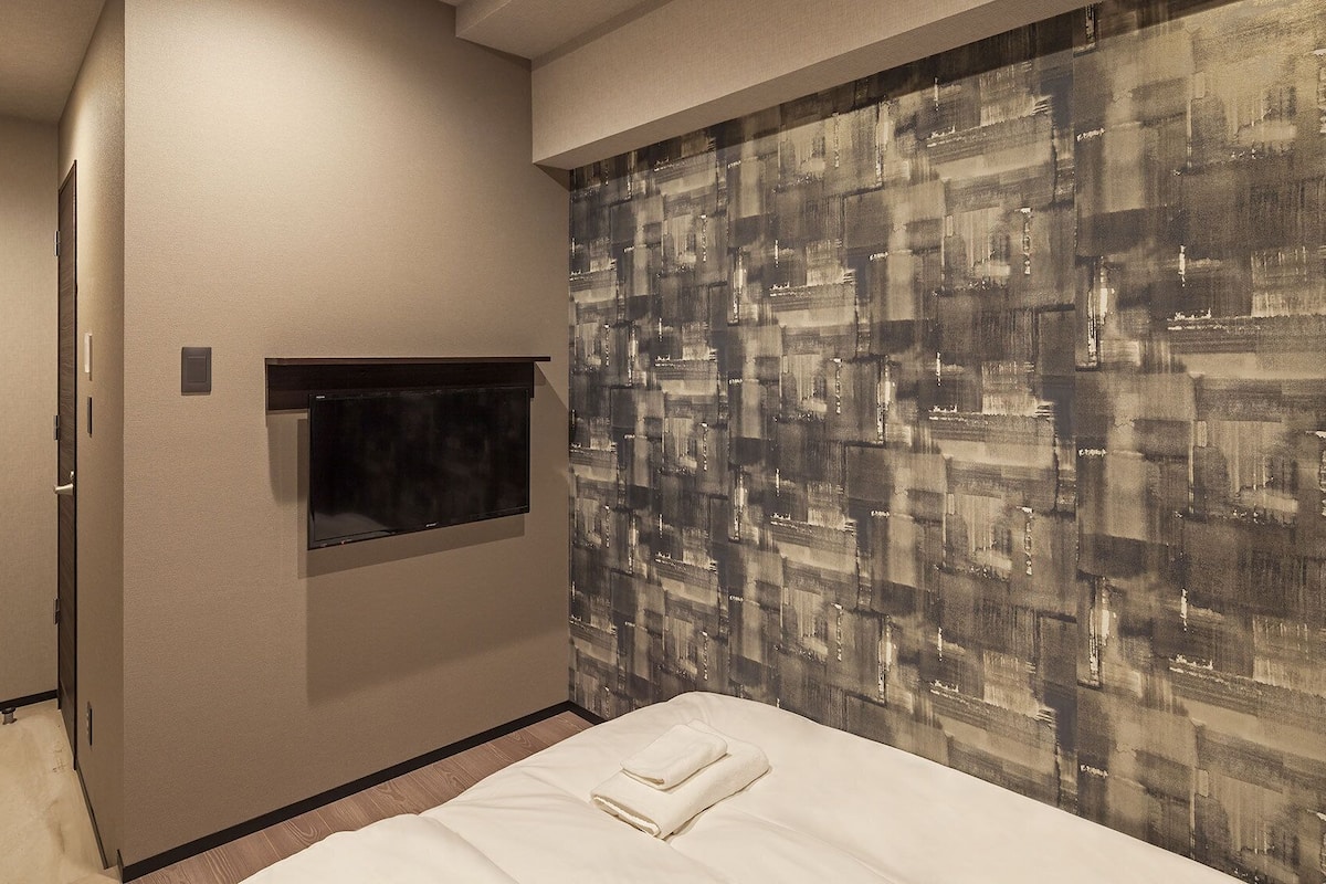 Une chambre d’hôtel avec un lit, un téléviseur à écran plat fixé au mur et un papier peint à motifs.