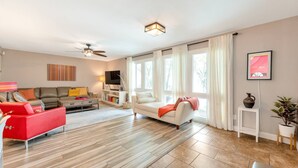 Un salon moderne avec un canapé, un fauteuil rouge, un téléviseur et un ventilateur de plafond.