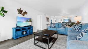 Una sala de estar con televisor, sofá azul, mesa de centro y decoración en la pared.