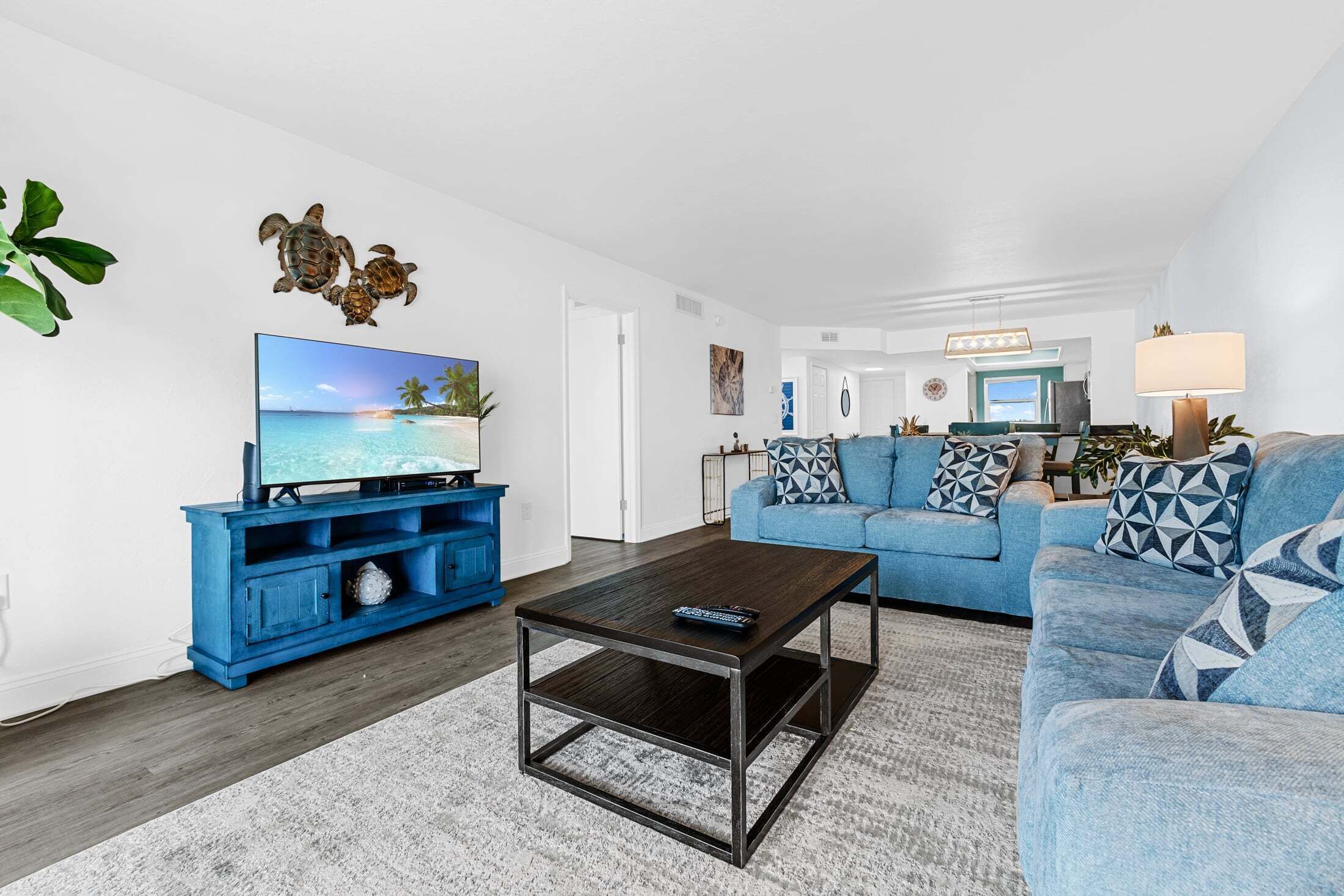 A living room with a TV, blue sofa, coffee table, and decorative wall art.