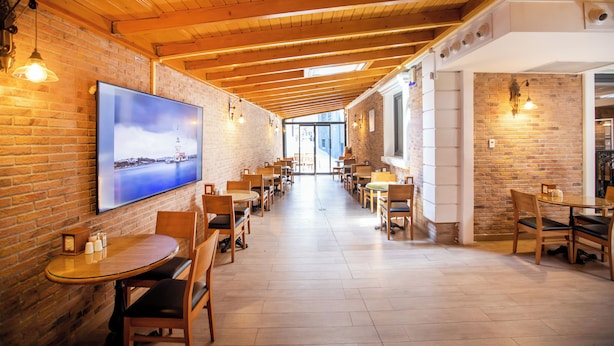 Um restaurante com paredes de tijolo, vigas de madeira no teto e um balcão comprido com mesas e cadeiras.