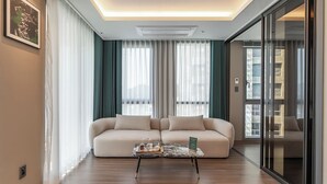 A modern living room with a beige sofa, a marble coffee table, and a large window with sheer curtains.