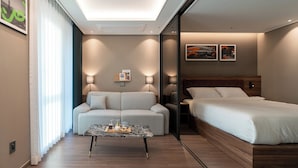 A modern hotel room with a sofa, a bed, a coffee table, and two wall-mounted lamps.