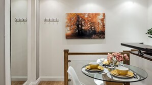 A dining area with a glass table set for four, a painting of autumn trees, and a plant on the right. - Mayfair Park Lane Lux 2-bedroom Apartment (London)