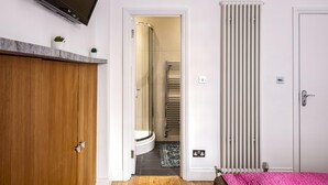 A modern bathroom with a wooden wardrobe, a shower area, a radiator, and a pink rug. - Mayfair Park Lane Lux 2-bedroom Apartment (London)