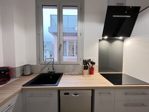 Een moderne keuken met een ingebouwde vaatwasser, een raam met uitzicht op gebouwen, en een afzuigkap.