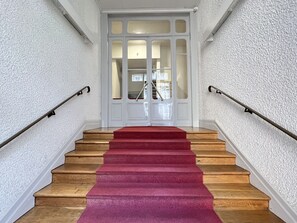 Een trap met houten treden en een rood tapijt, begrensd door witte muren en een witte deur met ruitpanelen.