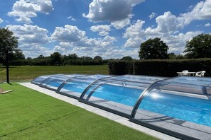 A swimming pool with a glass enclosure, surrounded by a well-maintained lawn and a hedge.
