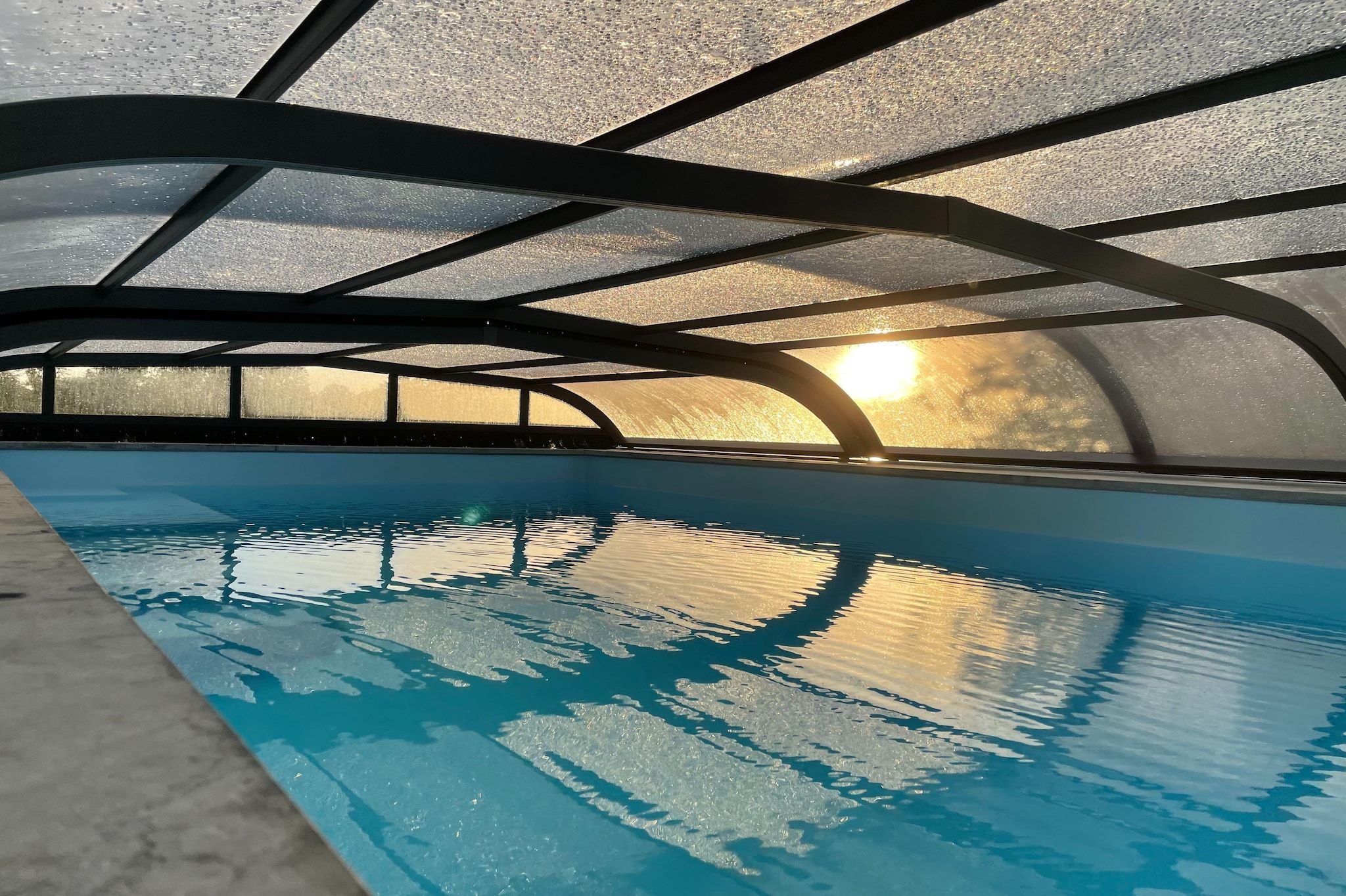 An indoor swimming pool with a clear view of the sun setting through a glass ceiling.