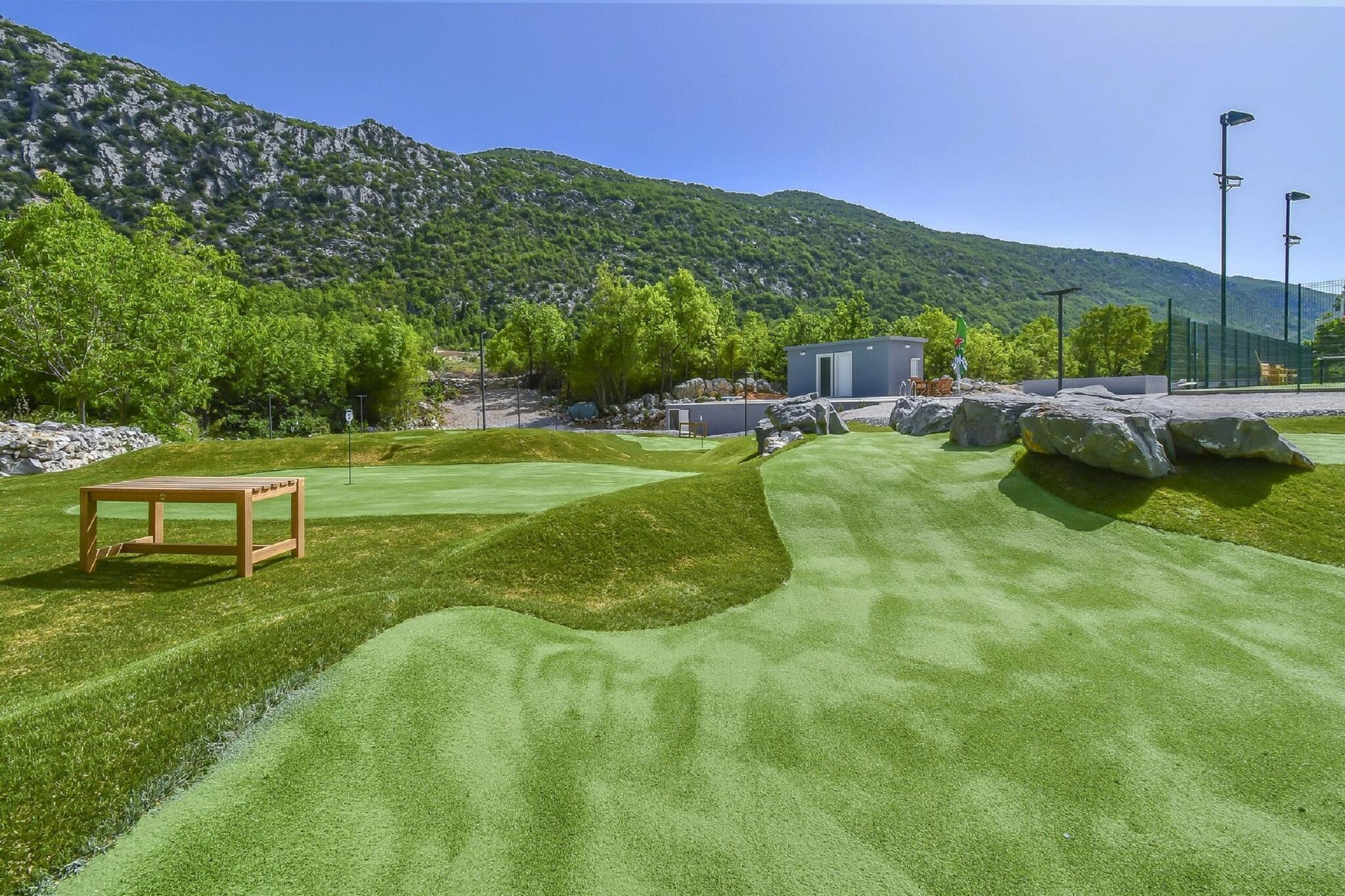 A golf course with a wooden bench, a small shed, and a mountain backdrop.