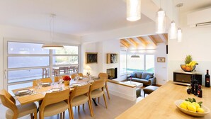 A modern kitchen with a wooden island, dining area with wooden chairs, and a view of the outdoors.