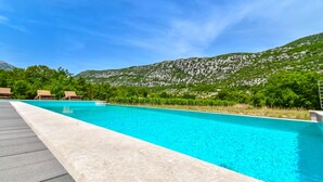 A swimming pool with clear blue water, surrounded by a deck and lounge chairs, with a mountainous backdrop.