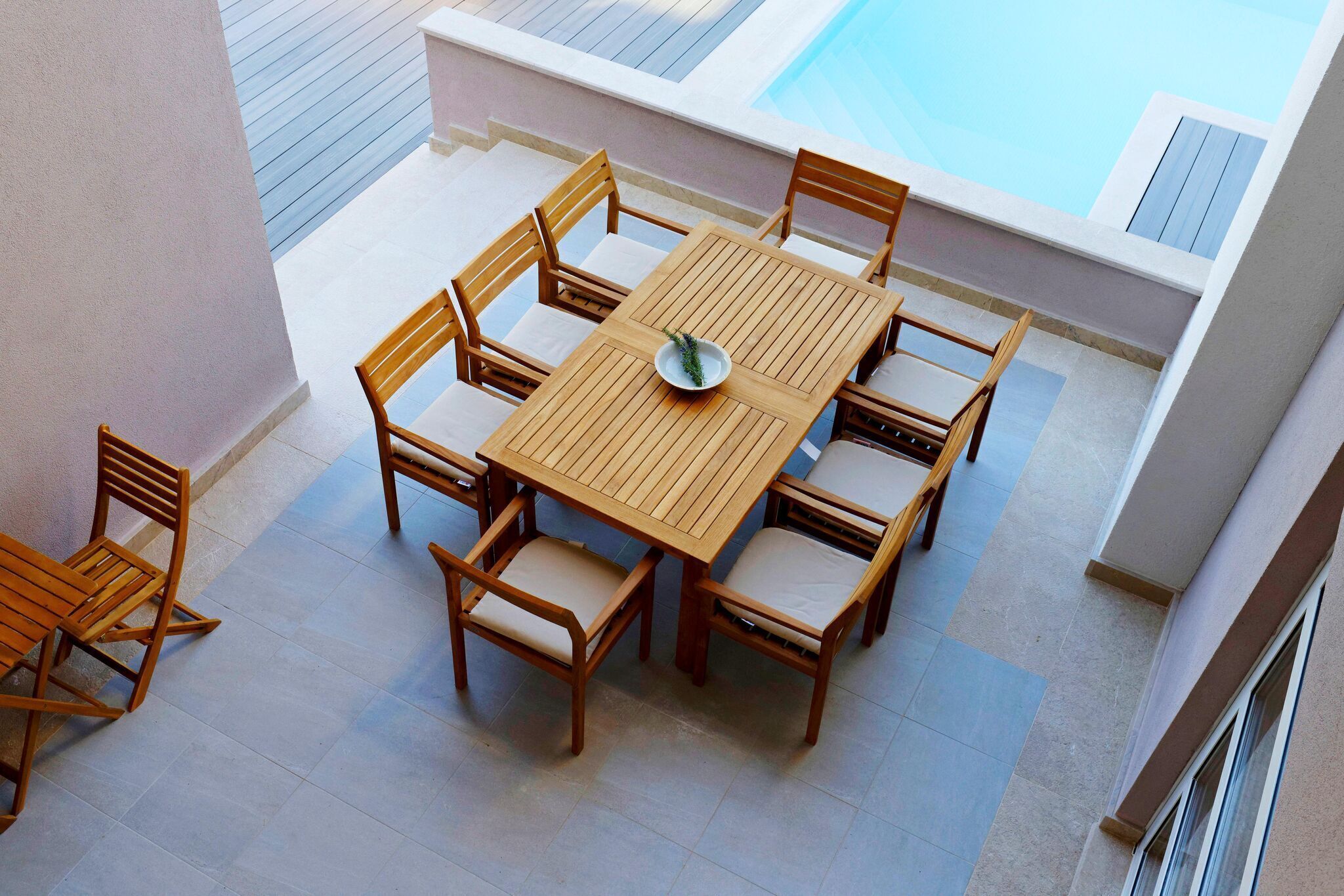 Une table et des chaises en bois sont disposées sur un balcon, avec une piscine en arrière-plan.