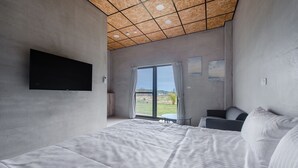 A modern bedroom with a large bed, a flat-screen TV, and a view of a garden through a sliding glass door. - sunisland (Liuqiu)