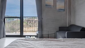 A bedroom with a large bed, a sofa, a small table, and a balcony with a view of the landscape. - sunisland (Liuqiu)