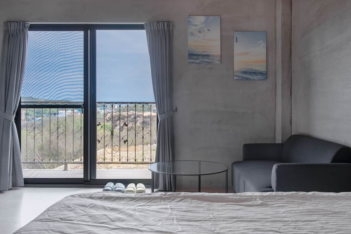 A bedroom with a large bed, a sofa, a small table, and a balcony with a view of the landscape.