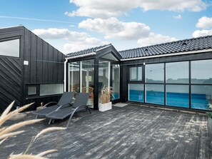Une terrasse extérieure moderne, dotée de chaises longues, d’une véranda en verre et offrant une vue sur la mer.