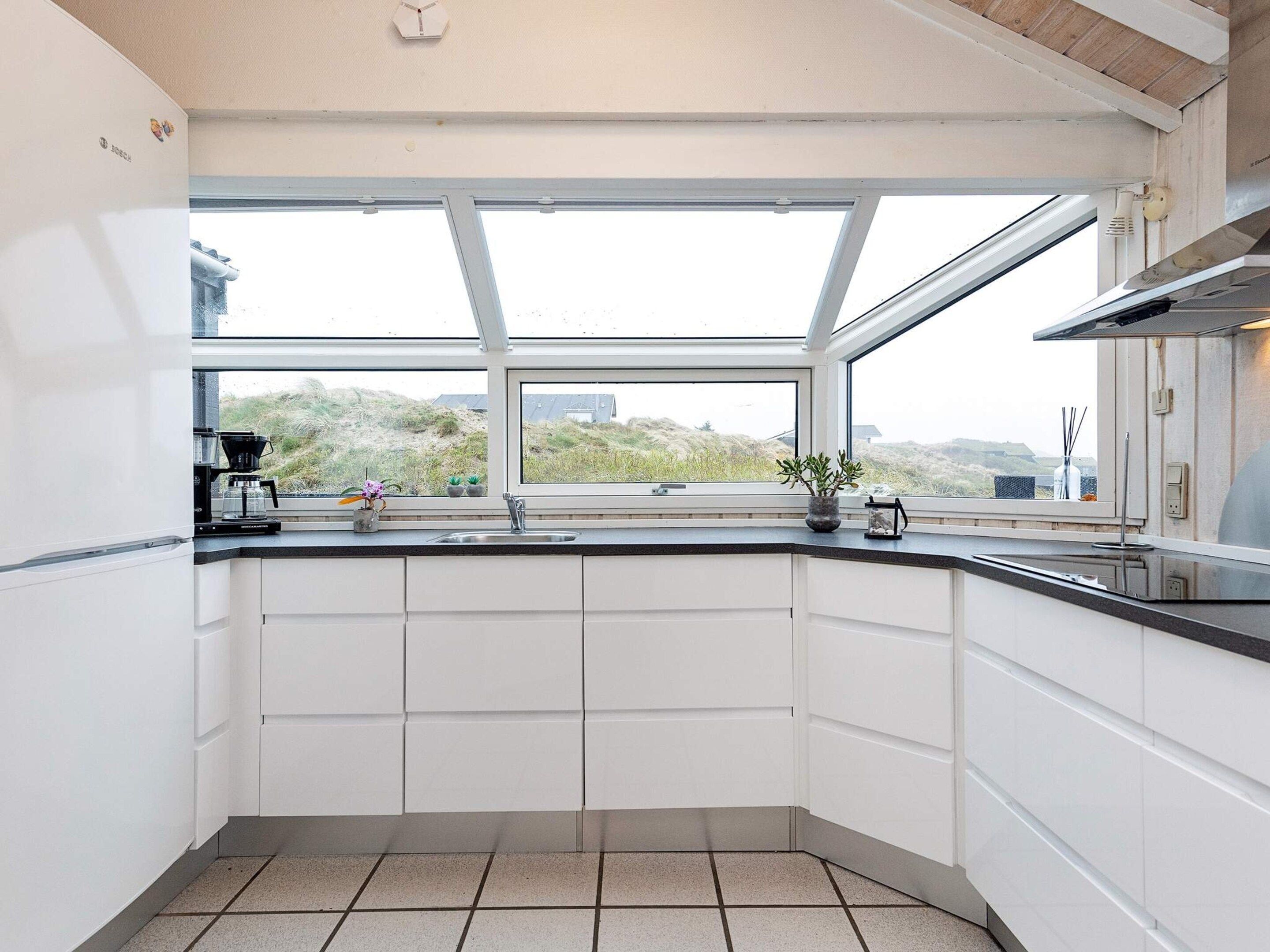 Een keuken met witte kasten, een zwart aanrecht en een groot raam met uitzicht op de omgeving.