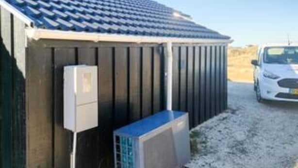 Un edificio con techo inclinado, un cuadro eléctrico y una unidad de aire acondicionado.