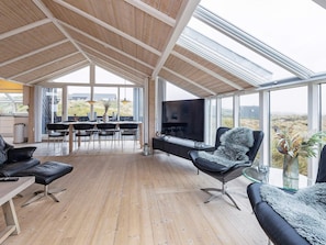A spacious living area with a wooden floor, a large TV, and comfortable seating.