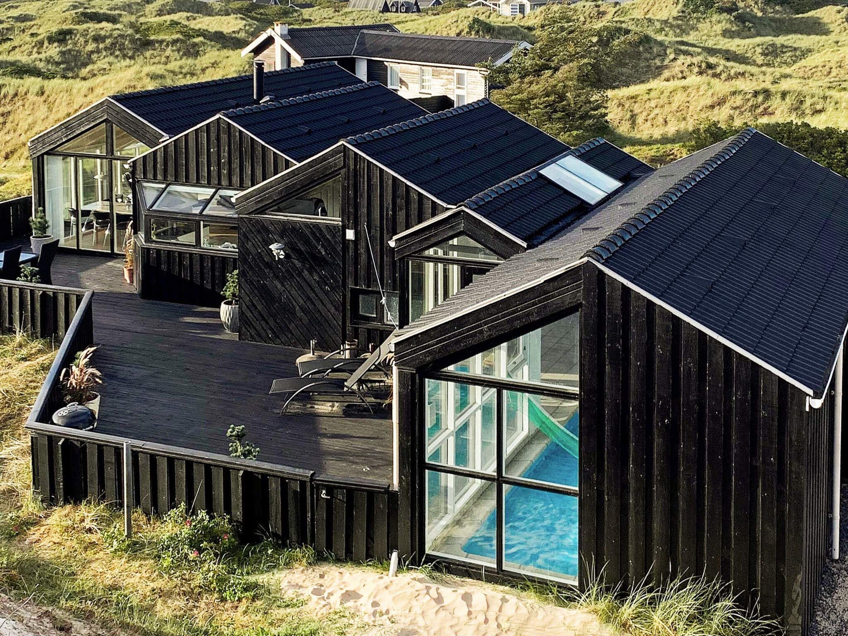 A modern wooden building with large windows and a flat roof, surrounded by natural landscape.