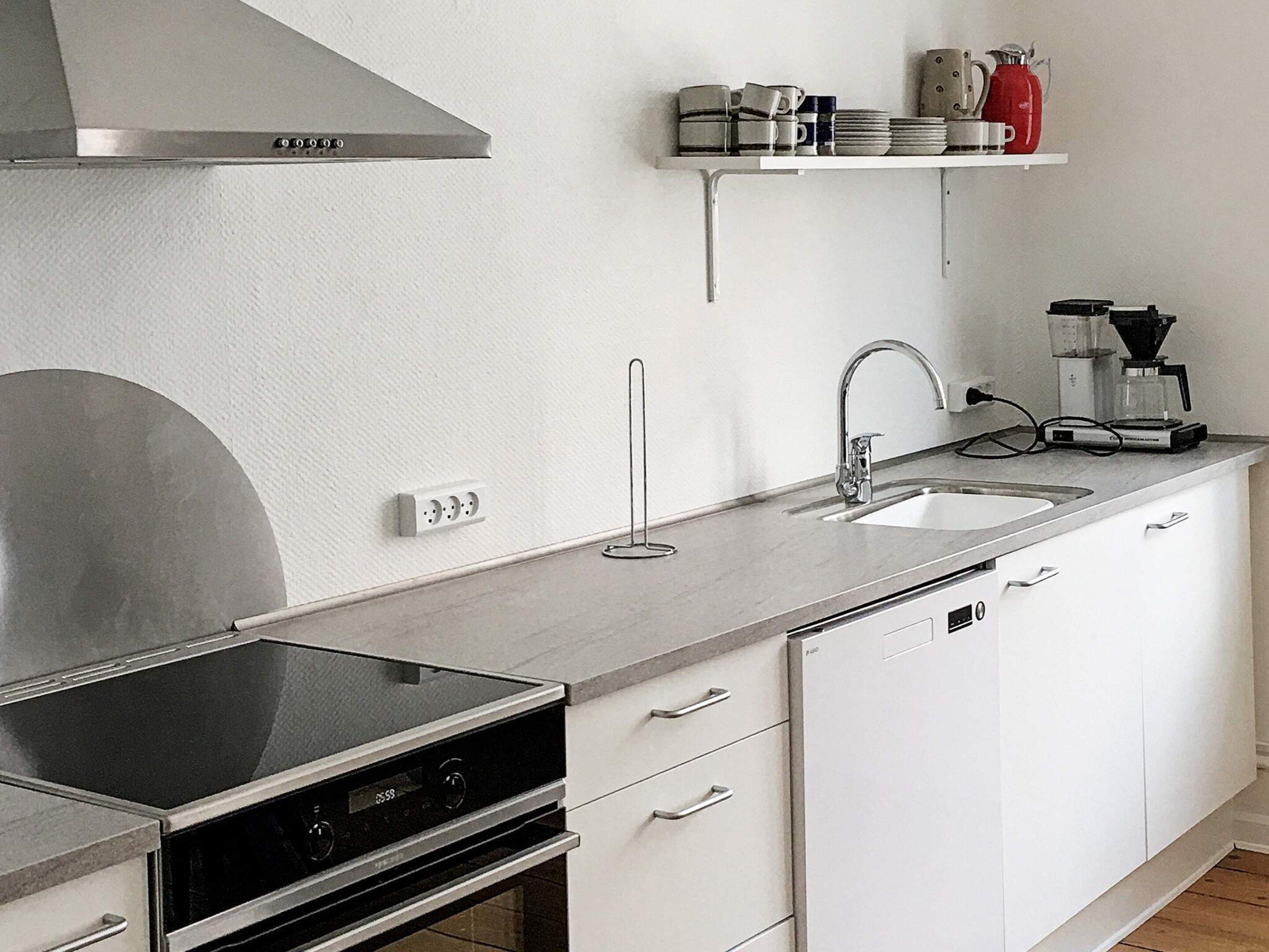 A modern kitchen with a built-in oven, a stainless steel range hood, a double sink, and a coffee maker on the countertop.