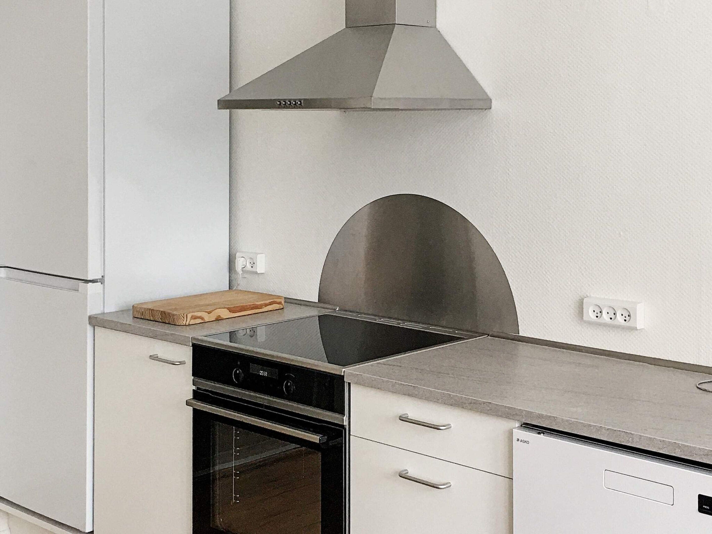 Een keuken met een roestvrijstalen afzuigkap, een inbouwoven en een aanrecht met een snijplank.
