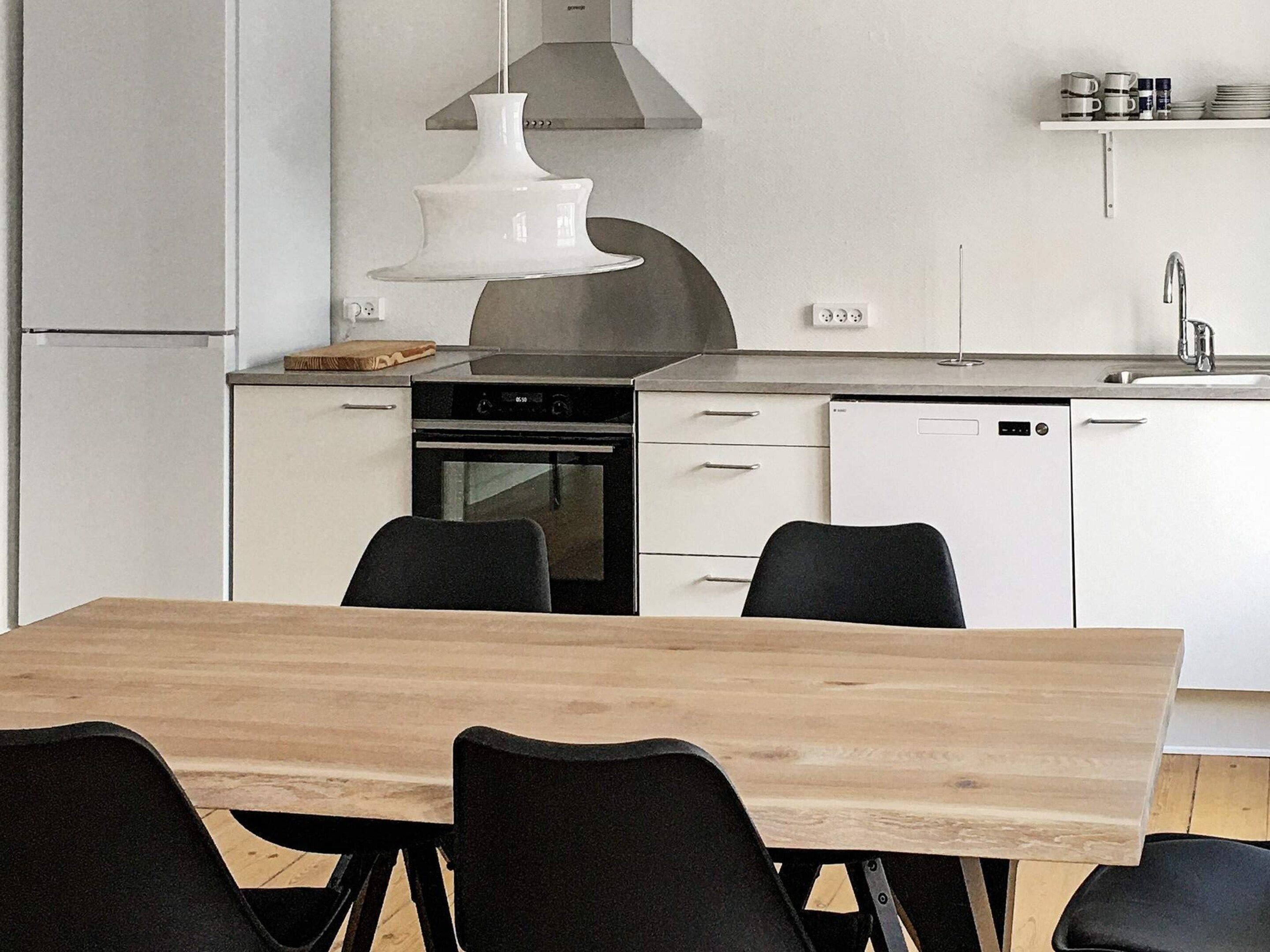 Een moderne keuken met witte kastjes, een roestvrijstalen afzuigkap, een vaatwasser en een eettafel met stoelen.