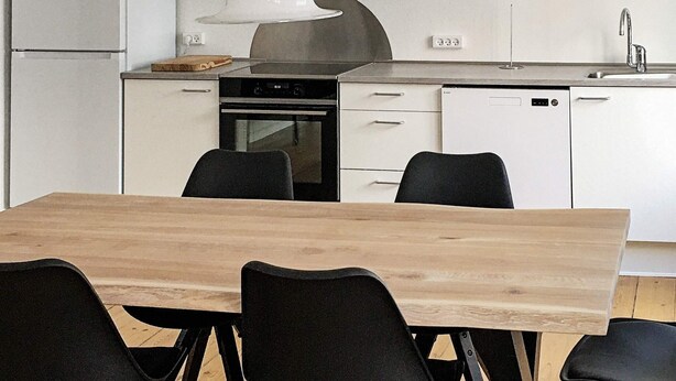 A modern kitchen with white cabinets, a stainless steel range hood, a dishwasher, and a dining table with chairs. - 5 Star Holiday Home in Nakskov (Nakskov)