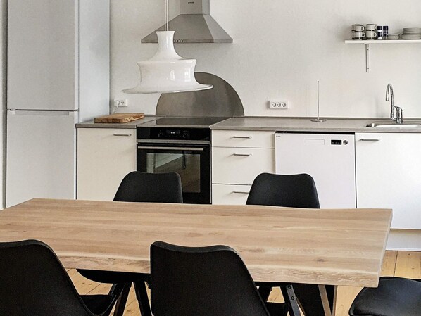 A modern kitchen with white cabinets, a stainless steel range hood, a dishwasher, and a dining table with chairs.