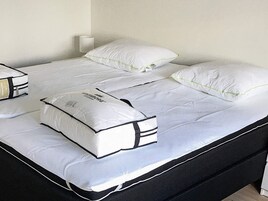 Una cama con ropa de cama blanca y dos almohadas, una pared blanca y una mesita de noche blanca.