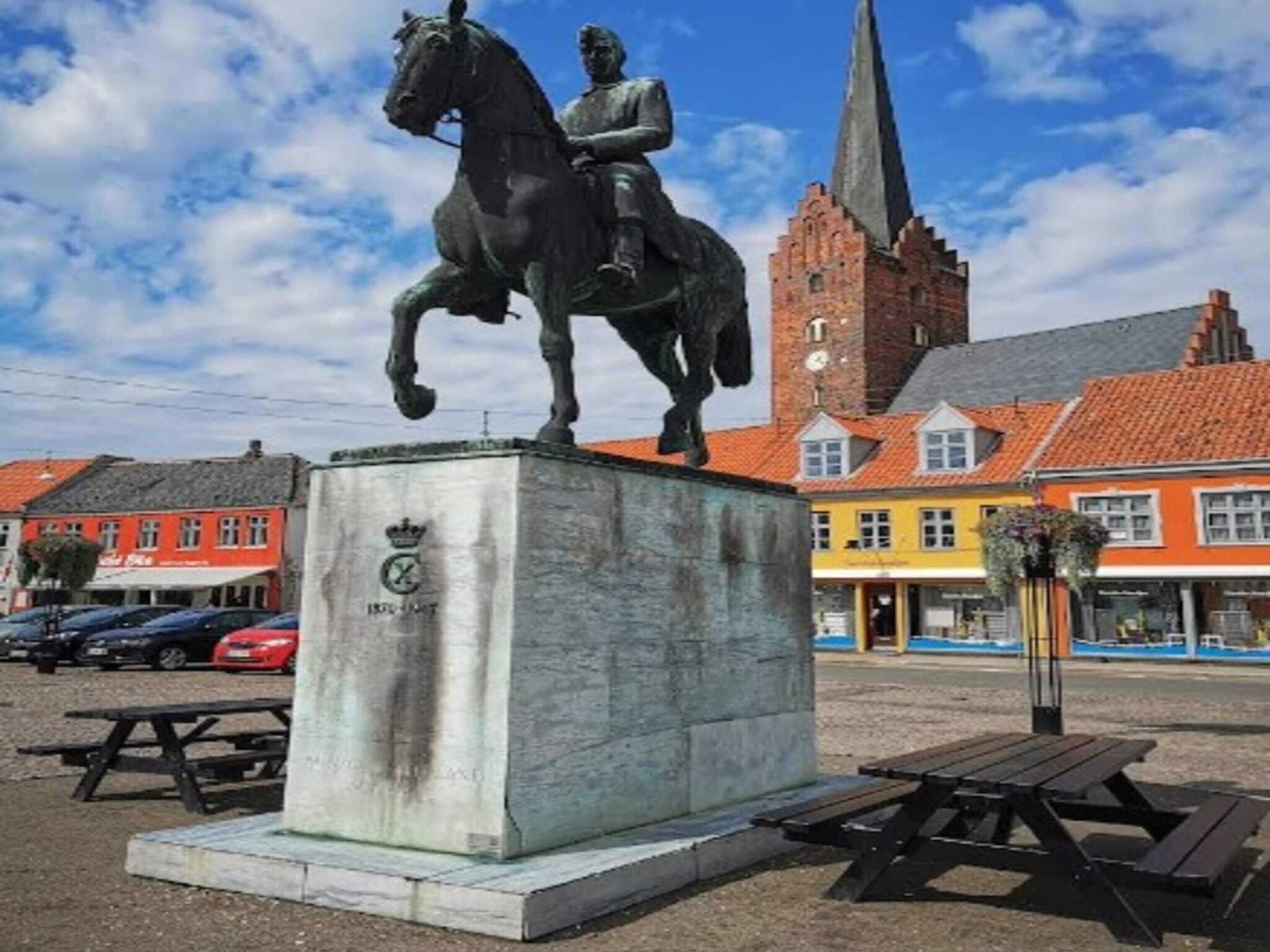 A statue of a man on a horse in a public square with a church in the background.